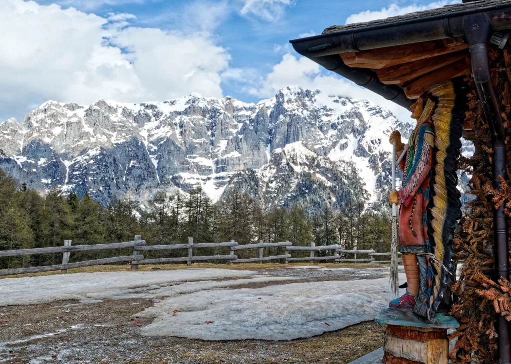 Una statua indiana come decorazione di una delle malghe trentine con dietro il panorama montano.
