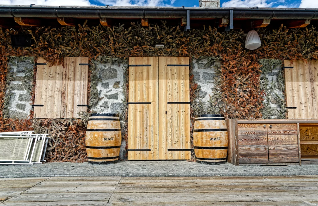 L'ingresso di una malga con ai lati due enormi barili. Tutto fatto in legno.
